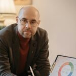 A professional man in an office setting presenting a circle graph on a clipboard.