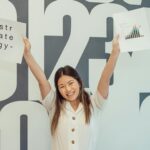 Smiling woman raises hands with strategy and graph papers, celebrating business success.