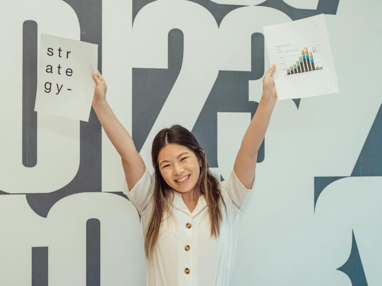 Smiling woman raises hands with strategy and graph papers, celebrating business success.